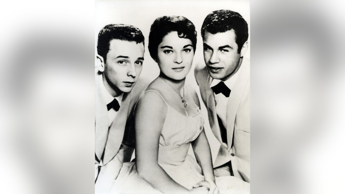 Carol Connors sitting in a gown in between her bandmates from the Teddy Bears.