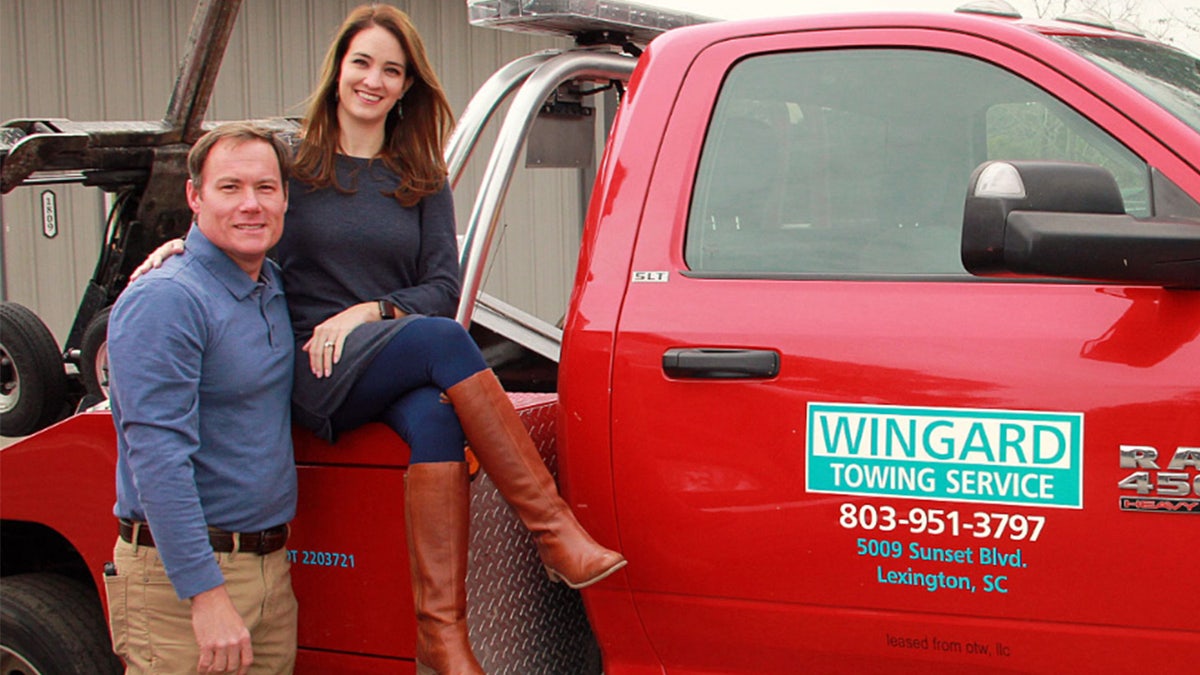 Woman poses with husband in front of a tow truck.