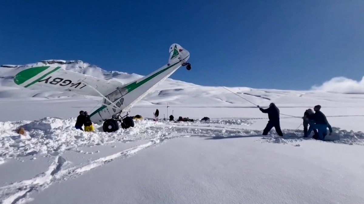 A rescue crew pulls a small plane back to its correct posture after it landed on a snowy mountain.