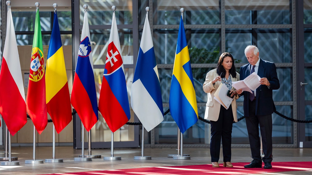 European Union foreign policy chief Josep Borrell, right, and a colleague, left, read a document next to the flags of EU member nations on a red carpet.