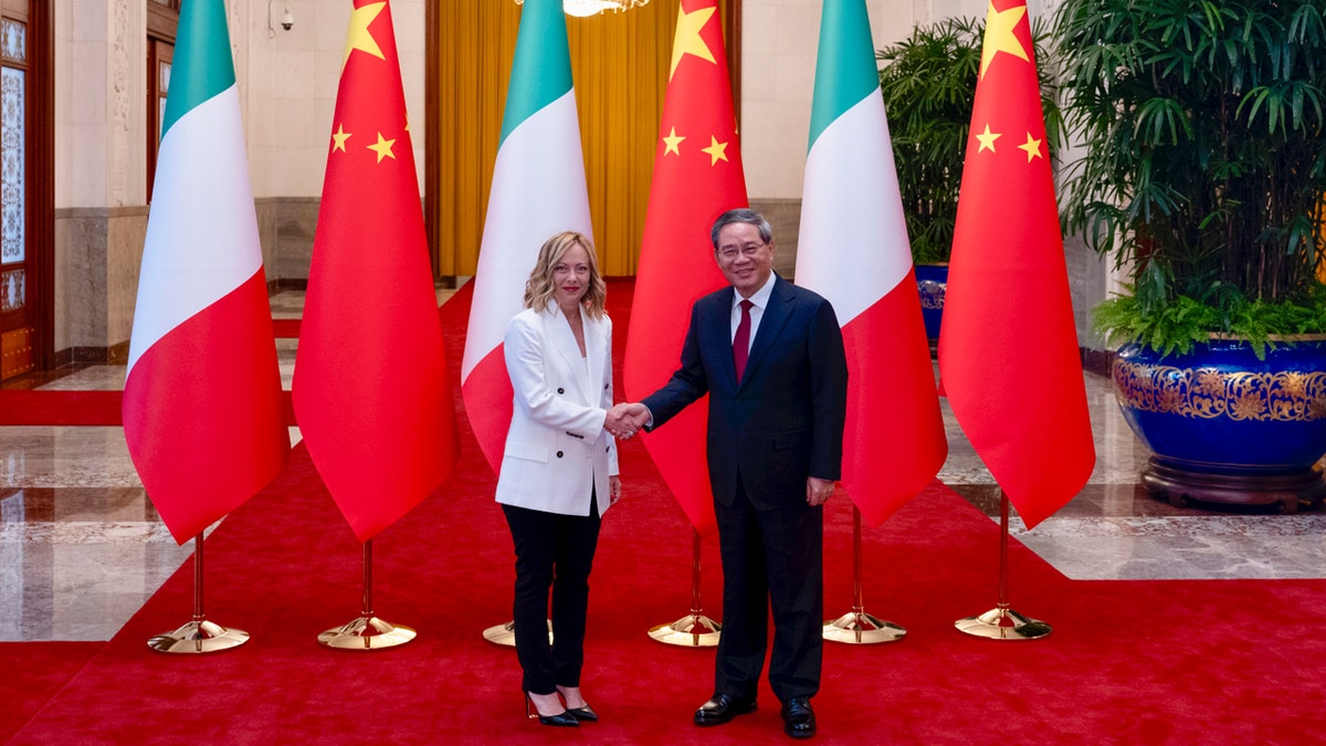 Italy's Prime Minister Giorgia Meloni shakes hands with Chinese Premier Li Qiang in front of Italian and Chinese flags