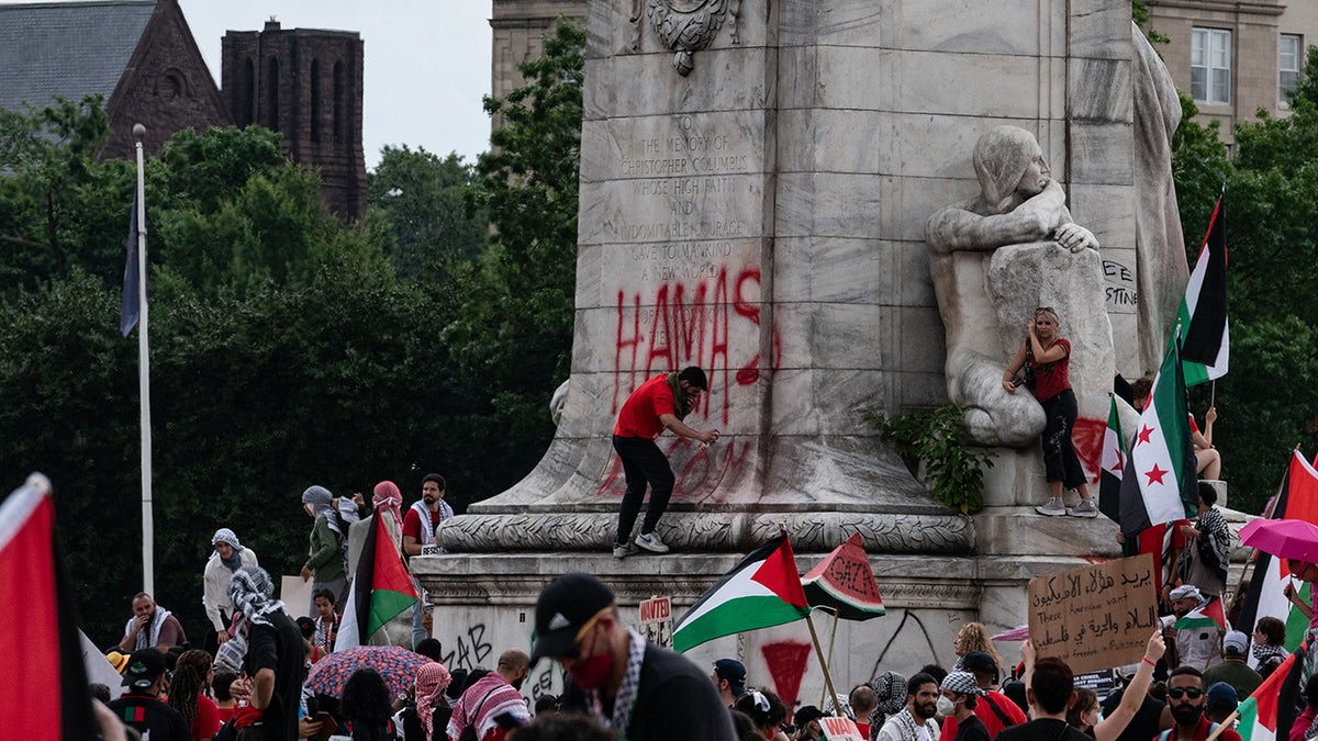 A person spray paints on the base of the Christopher Columbus Memorial Fountain as pro-Palestinian demonstrators protest near the US Capitol