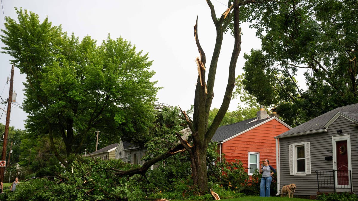 A woman stands outside her home after a severe storm took down trees in Iowa.
