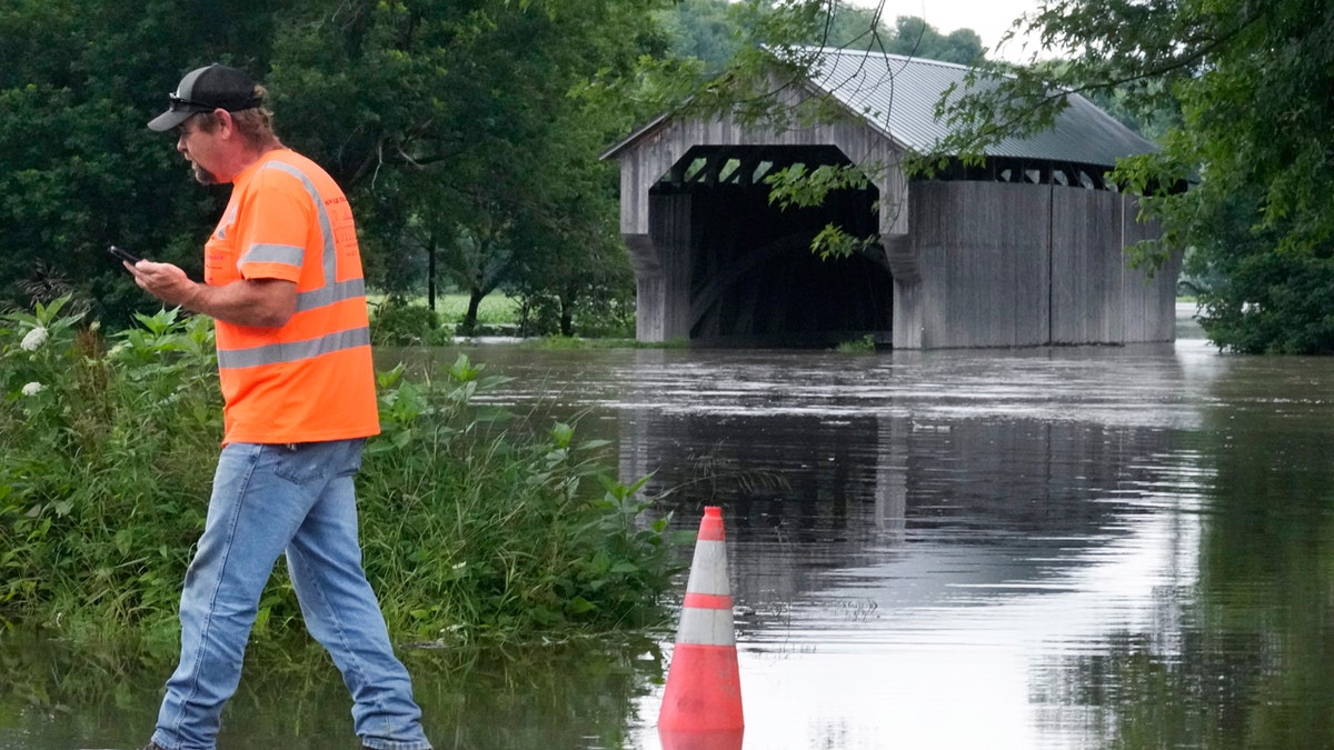 An employee of the Vermont Transportation Agency walks past the Gates Farm Covered Bridge, now flooded.
