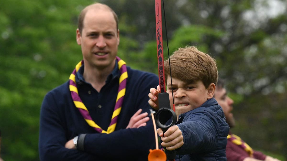 prince george using bow and arrow as prince william looks on