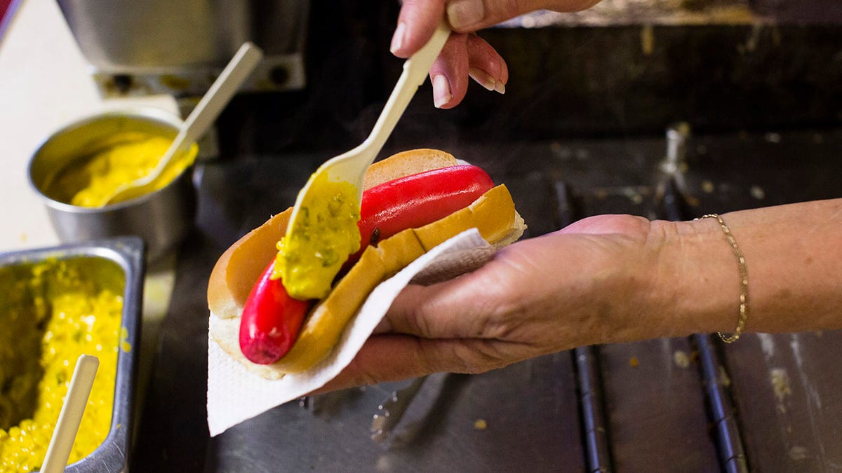 Person putting mustard on an extremely red hot dog.