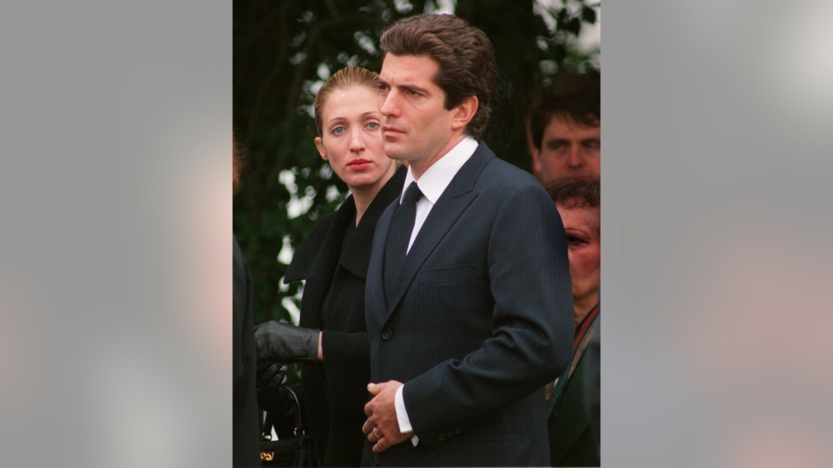 Carolyn Bessette-Kennedy looking on as John F. Kennedy wearing a dark suit as he looks tense.
