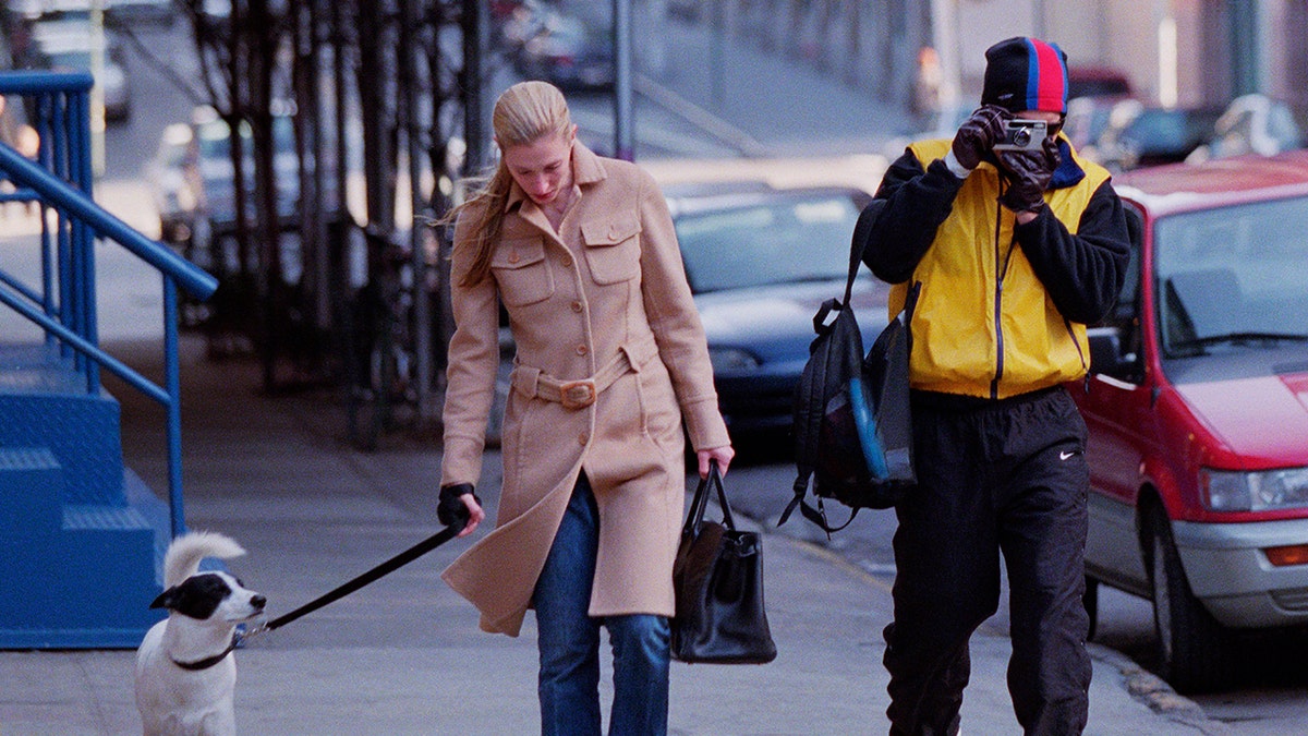 A paparazzo photographing Carolyn Bessette-Kennedy outside as she walks her dog.