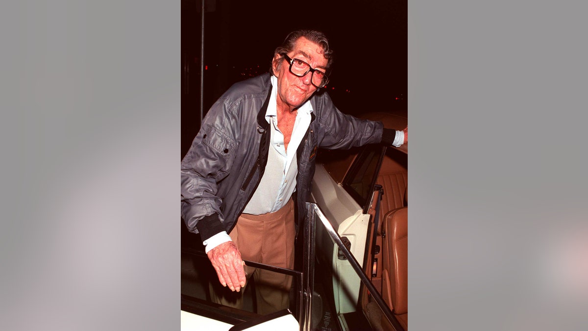 Dean Martin stepping out of a car in a blue leather jacket and brown pants