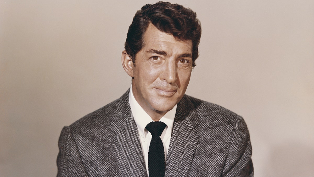 A close-up of Dean Martin wearing a gray suit and a black tie.