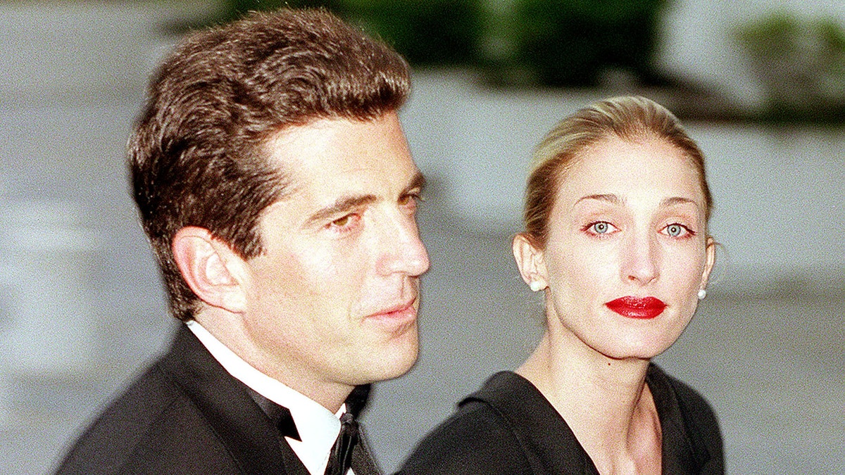 John F. Kennedy Jr. and Carolyn Bessette-Kennedy walking together at an event wearing formal wear.