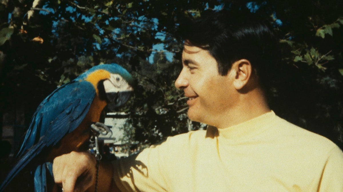 Jim Jones wearing a yellow shirt in the jungle admiring a parrot.