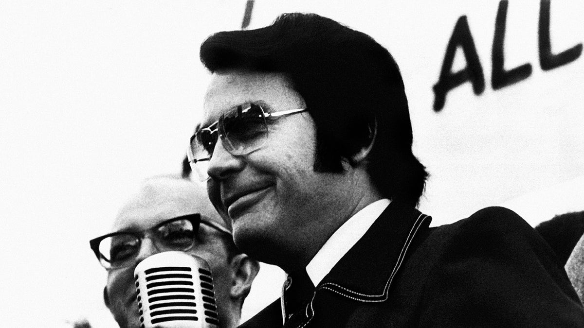 A close-up of Jim Jones speaking to a mic.