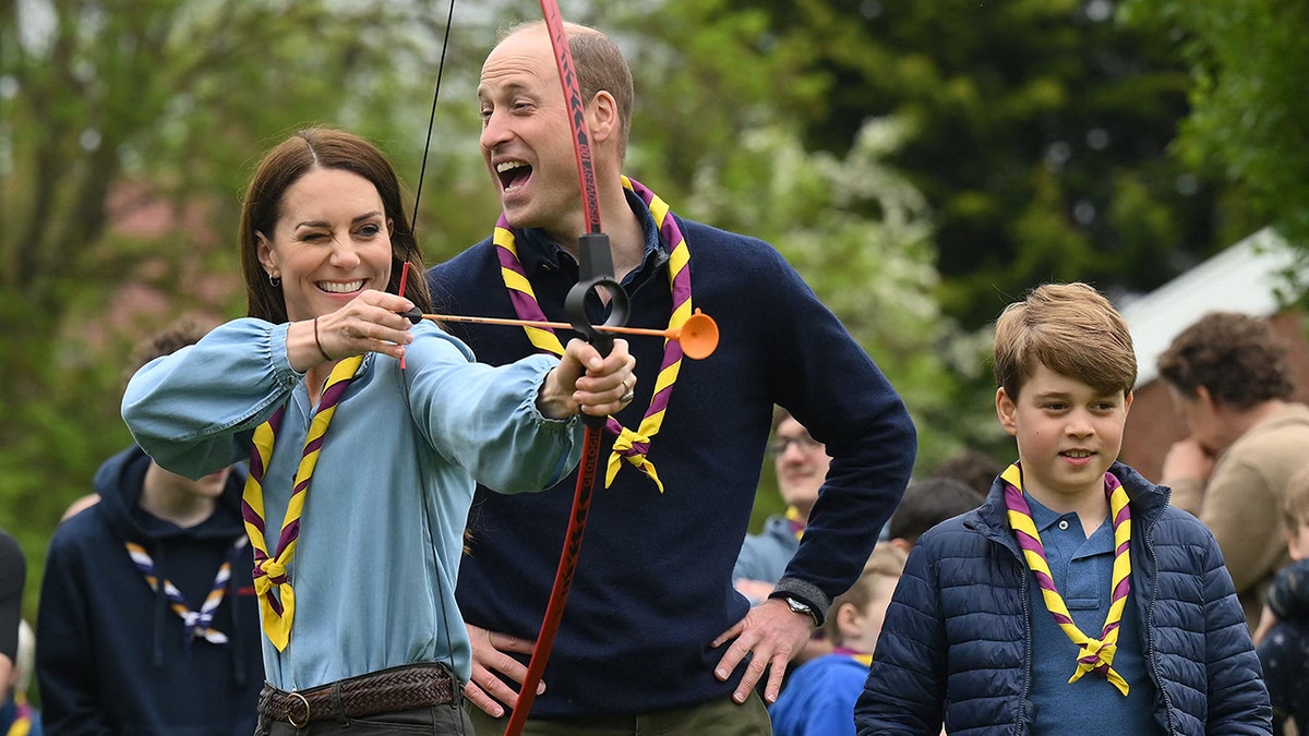 Kate Middleton preparing to shoot with a bow and arrow as Prince William and Prince George look on.
