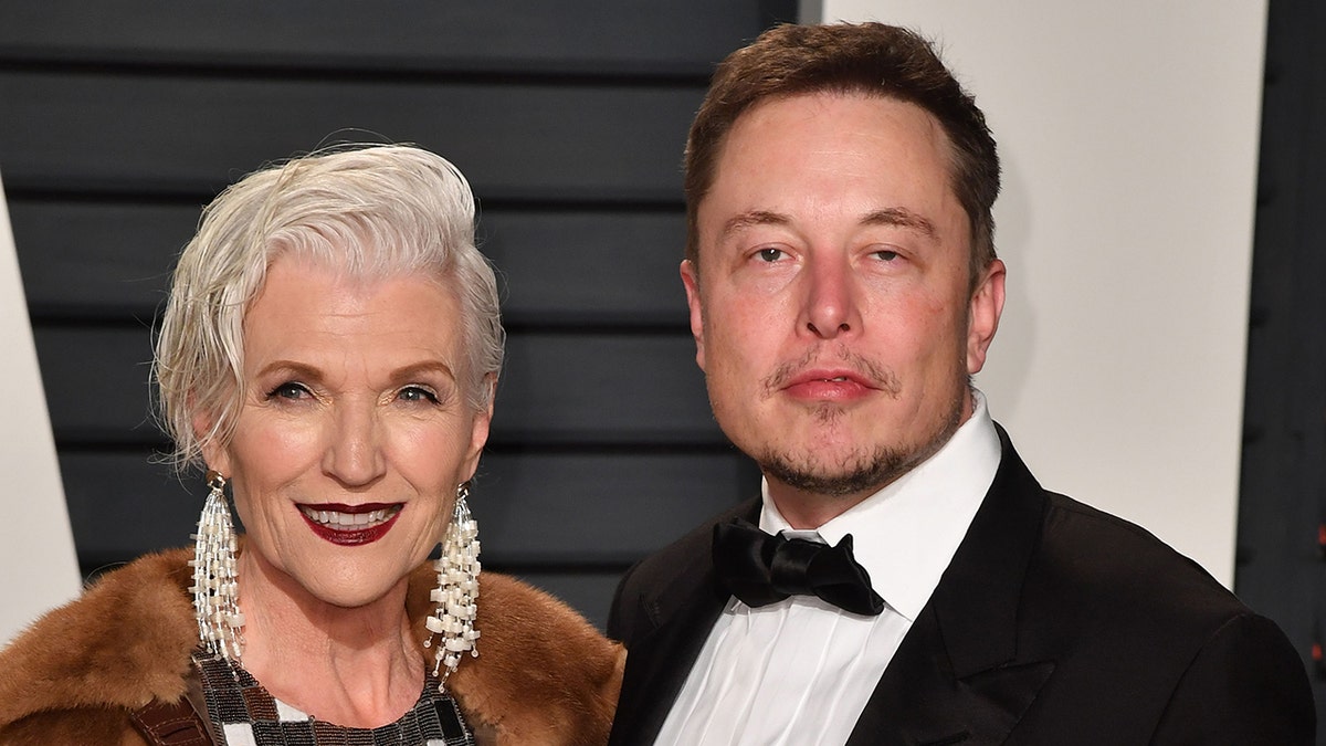 Maye Musk wearing a fur coat and posing next to Elon Musk in a suit and bow tie.