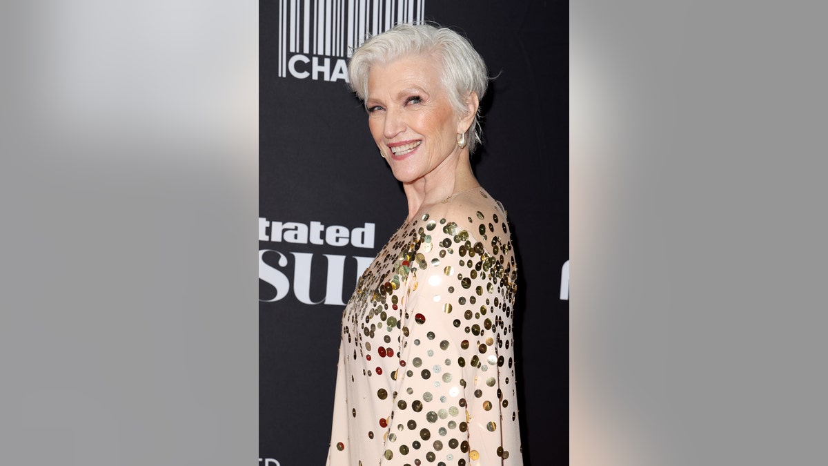 Maye Musk looking to the side and smiling in a gold and beige sparkling dress.