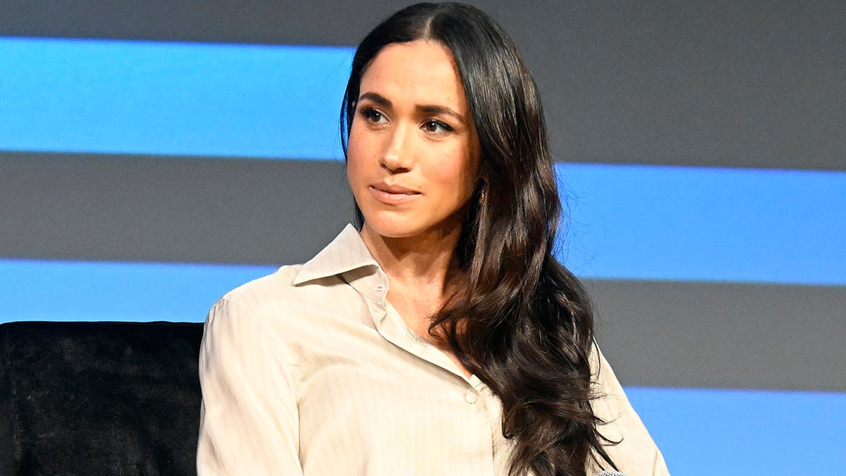 A close-up of Meghan Markle looking pensive in a beige blouse.