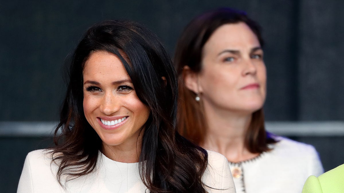 Samantha Cohen looking at Meghan Markle closely as the Duchess of Sussex smiles.
