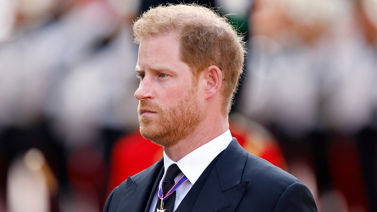 Prince Harry looking somber in a navy suit while wearing medals.