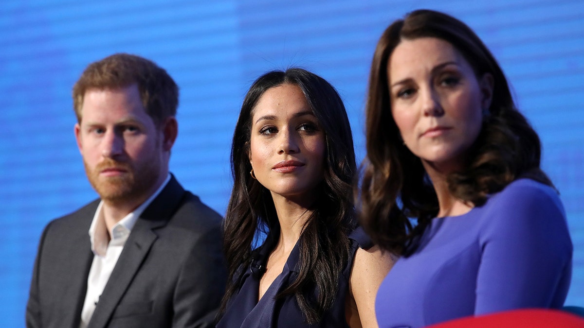 Prince Harry, Meghan Markle and Kate Middleton sitting next to each other facing the same direction.