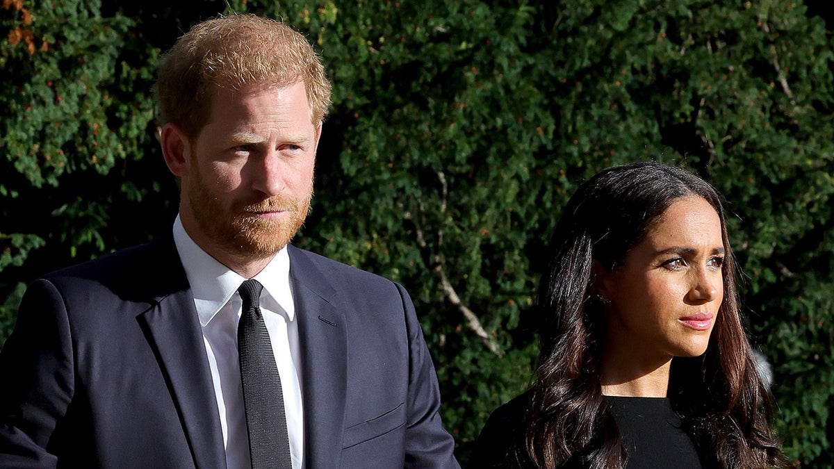 Prince Harry and Meghan Markle walking together looking somber