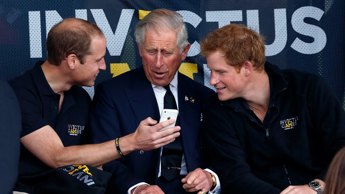 Prince William showing King Charles his phone as Prince Harry watches on.