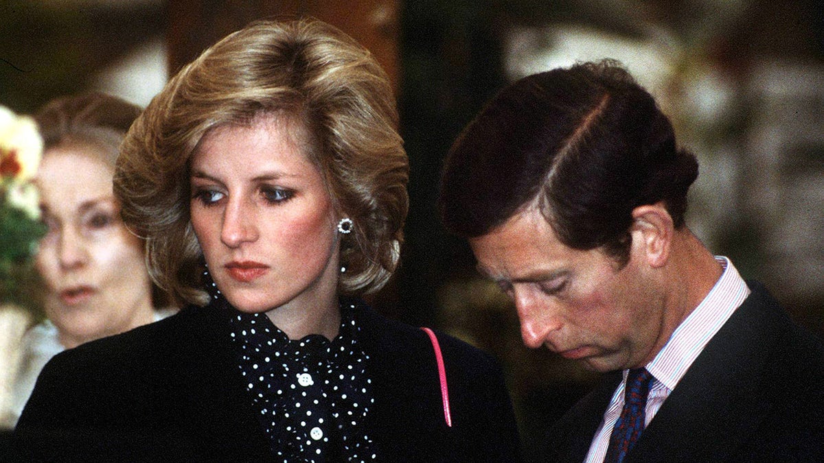 Prince Charles and Princess Diana looking disappointed in dark clothing.
