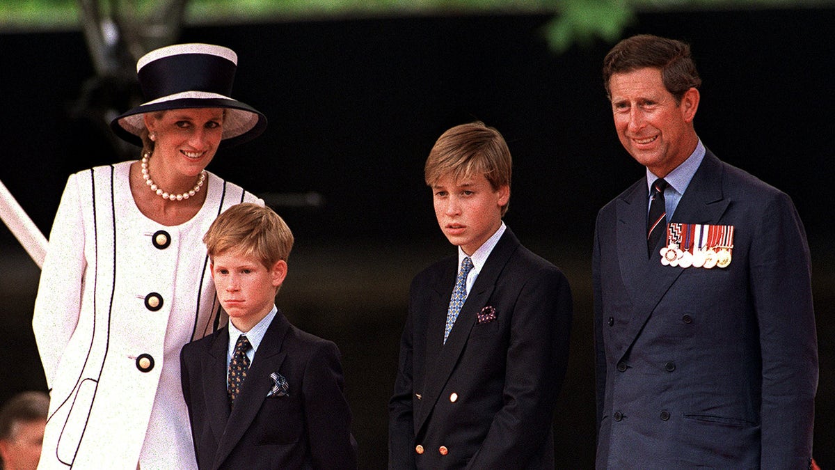 Princess Diana wearing a white and black striped dress with a matching hat standing next to her sons and Prince Charles in suits