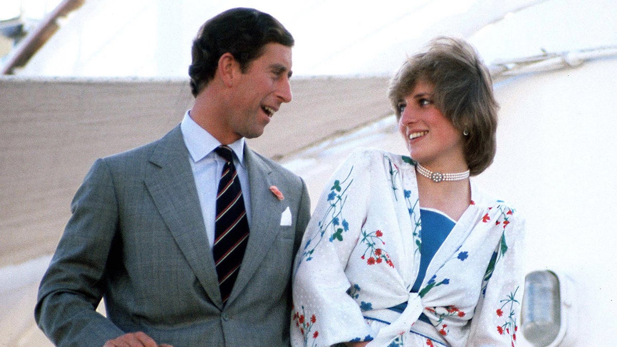 Prince Charles in a grey suit smiling and chatting with Diana in a white floral top with a blue blouse