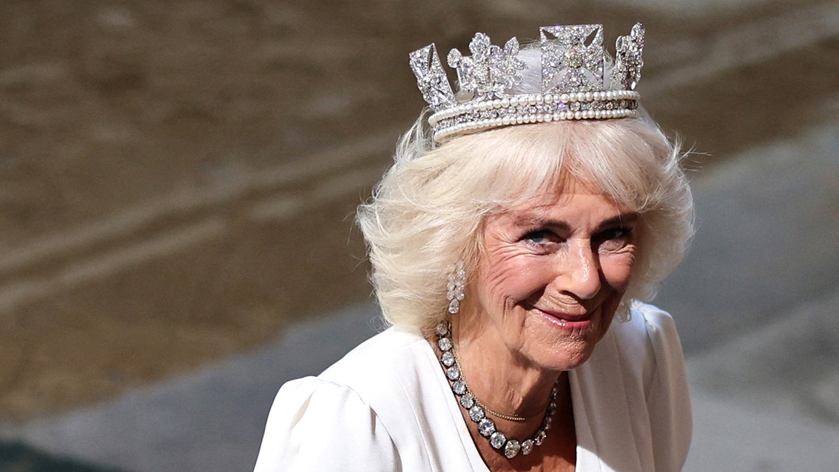 Queen Camilla smiling wearing a diamond encrusted crown and a white dress.