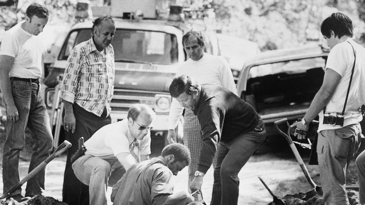 A close-up of police removing a body from a ditch.