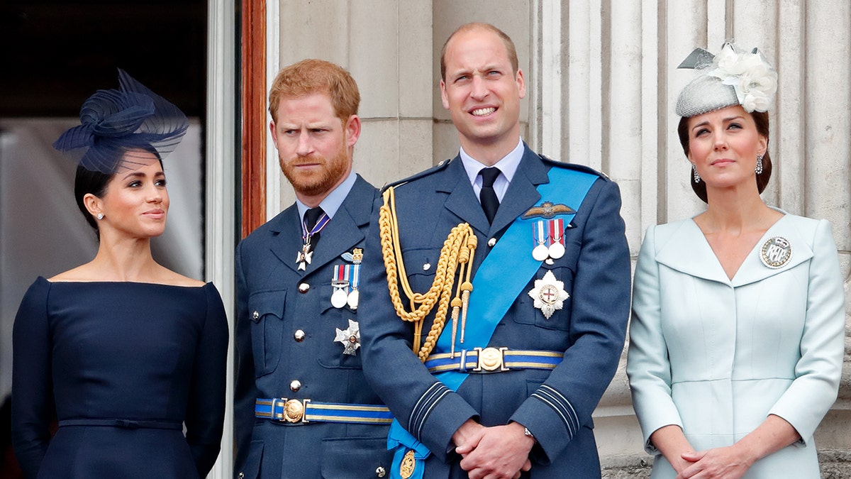 Prince William smiling with Prince Harry looking tense. Meghan Markle looks on as Kate Middleton stands next to her husband appearing serious.