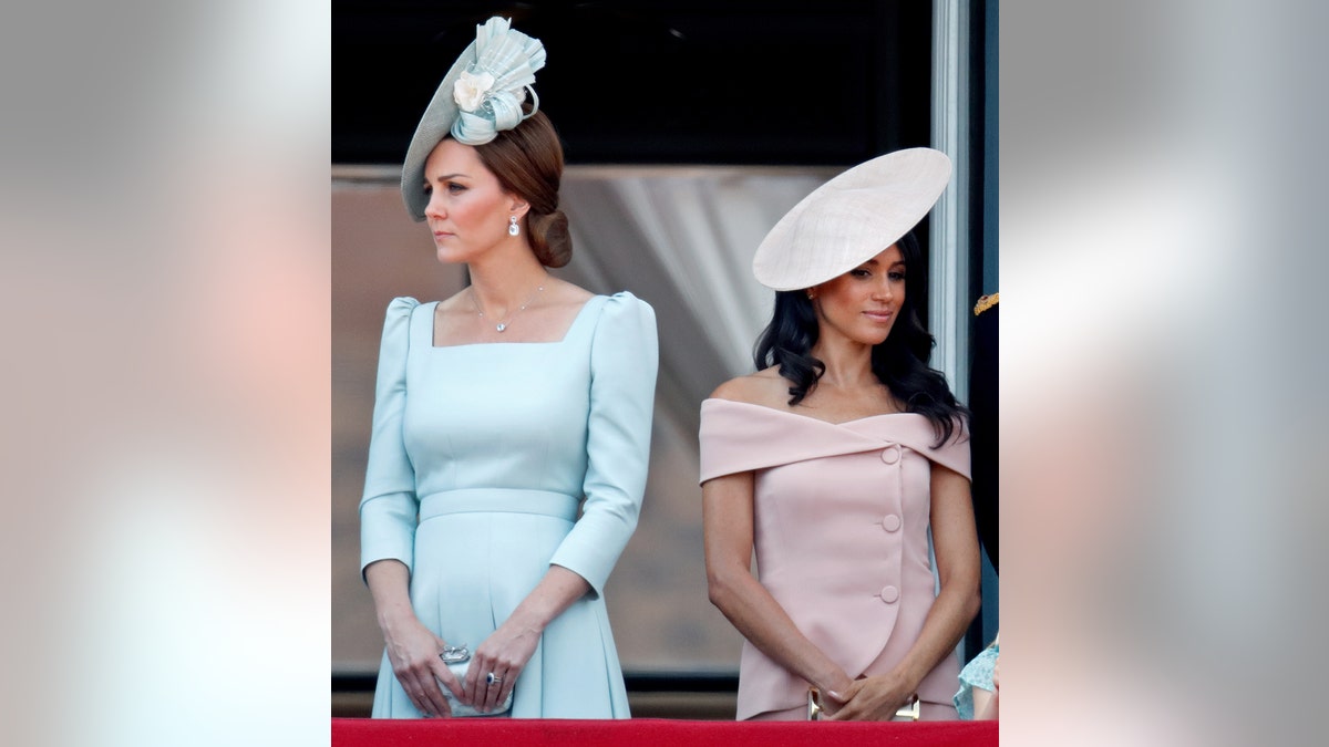 Kate Middleton in a light blue dress with her back turned away from Meghan Markle, who is wearing a pink dress.
