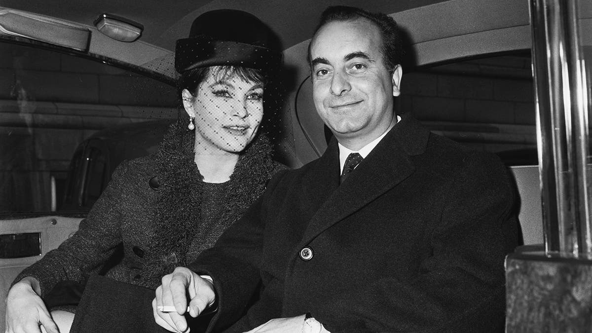 Yvonne Furneaux wearing a black dress with a matching hat sitting next to her husband