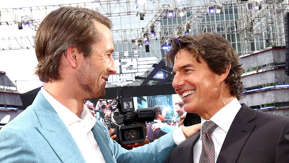 Glen Powell putting his hand on Tom Cruise's shoulder