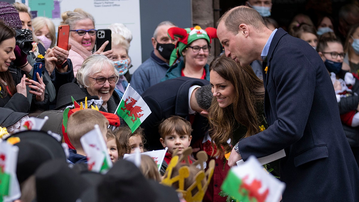 Prince William and Kate Middleton in a crowd of people waving Welsh flags