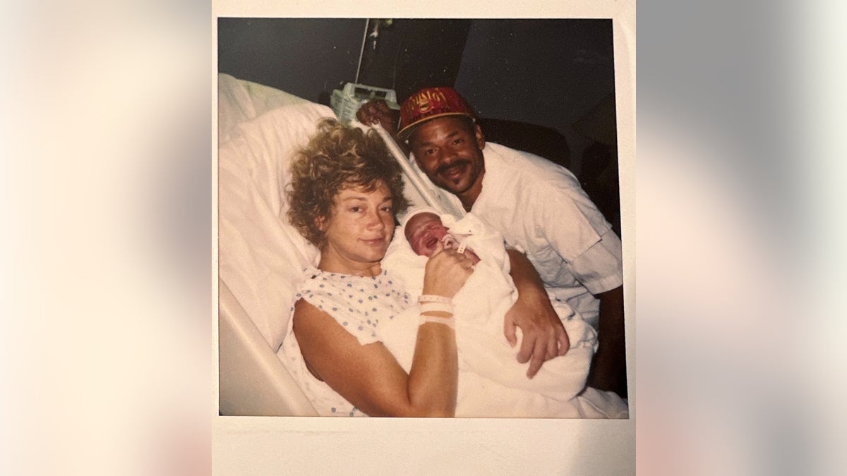 Madison McGhees mother holding her as a baby in the hospital with J.C. leaning in.