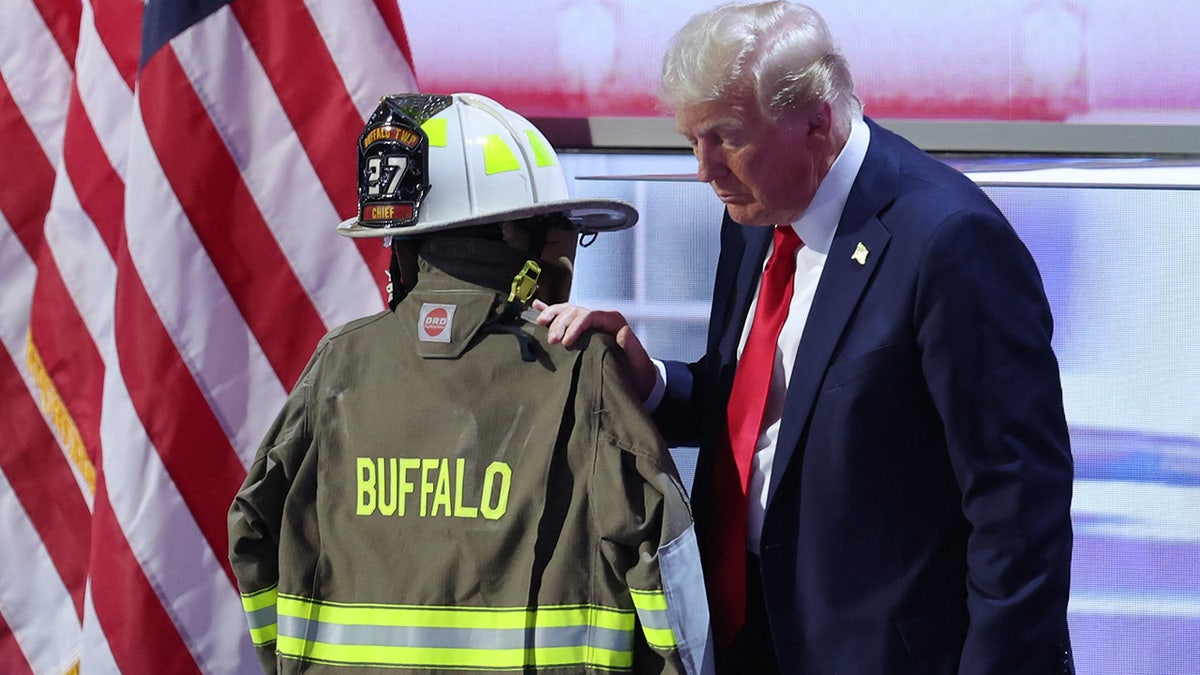 Republican presidential nominee and former U.S. President Donald Trump touches the turnout coat of former Buffalo Township Volunteer Fire Department chief Corey Comperatore, who was killed at his rally, on Day 4 of the Republican National Convention (RNC), at the Fiserv Forum in Milwaukee, Wisconsin, U.S., July 18, 2024. 