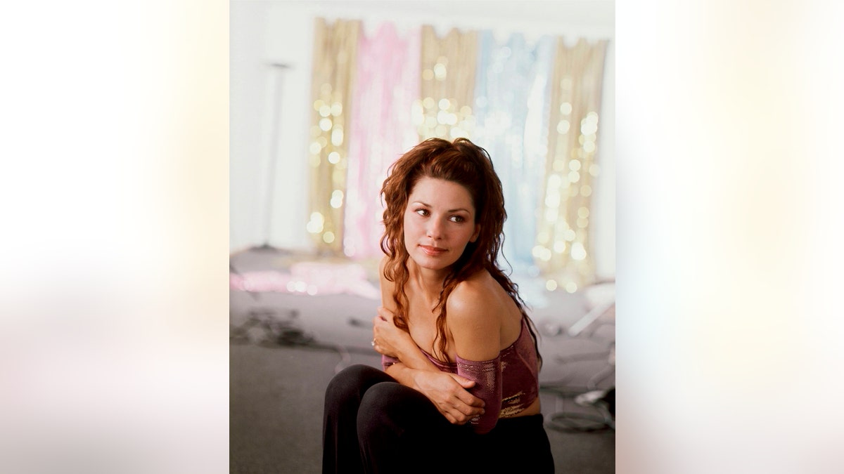 Shania Twain sitting down holding her arms across her chest in promo photo