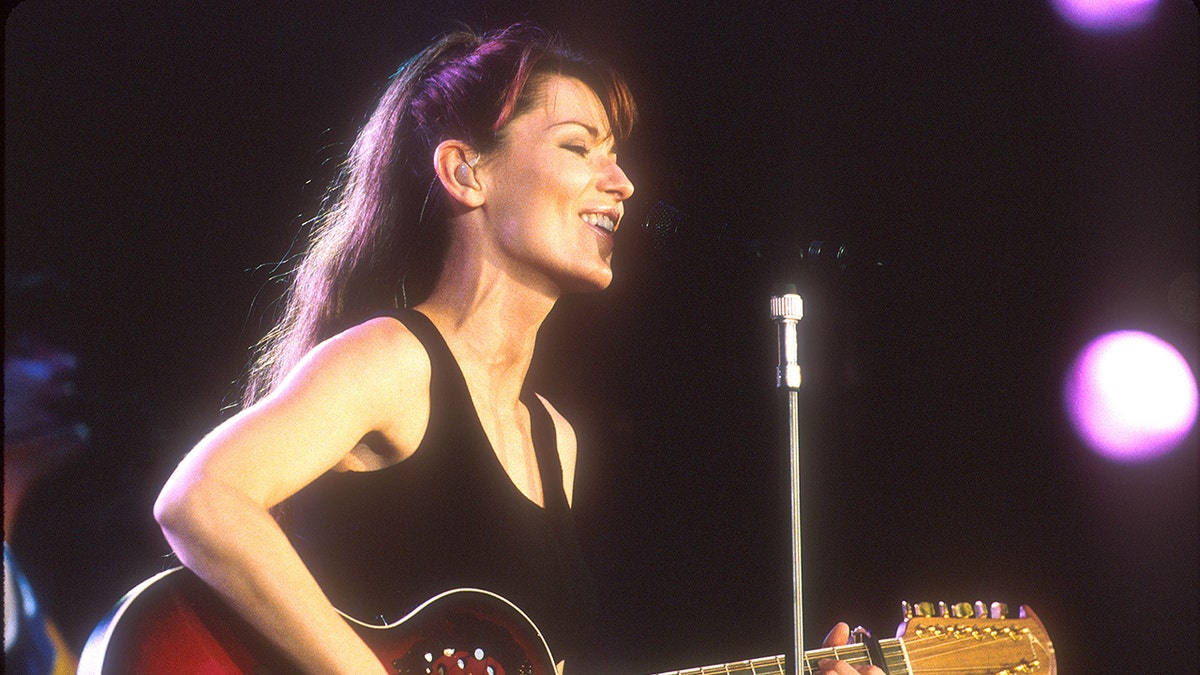 Shania Twain playing guitar and singing into a microphone