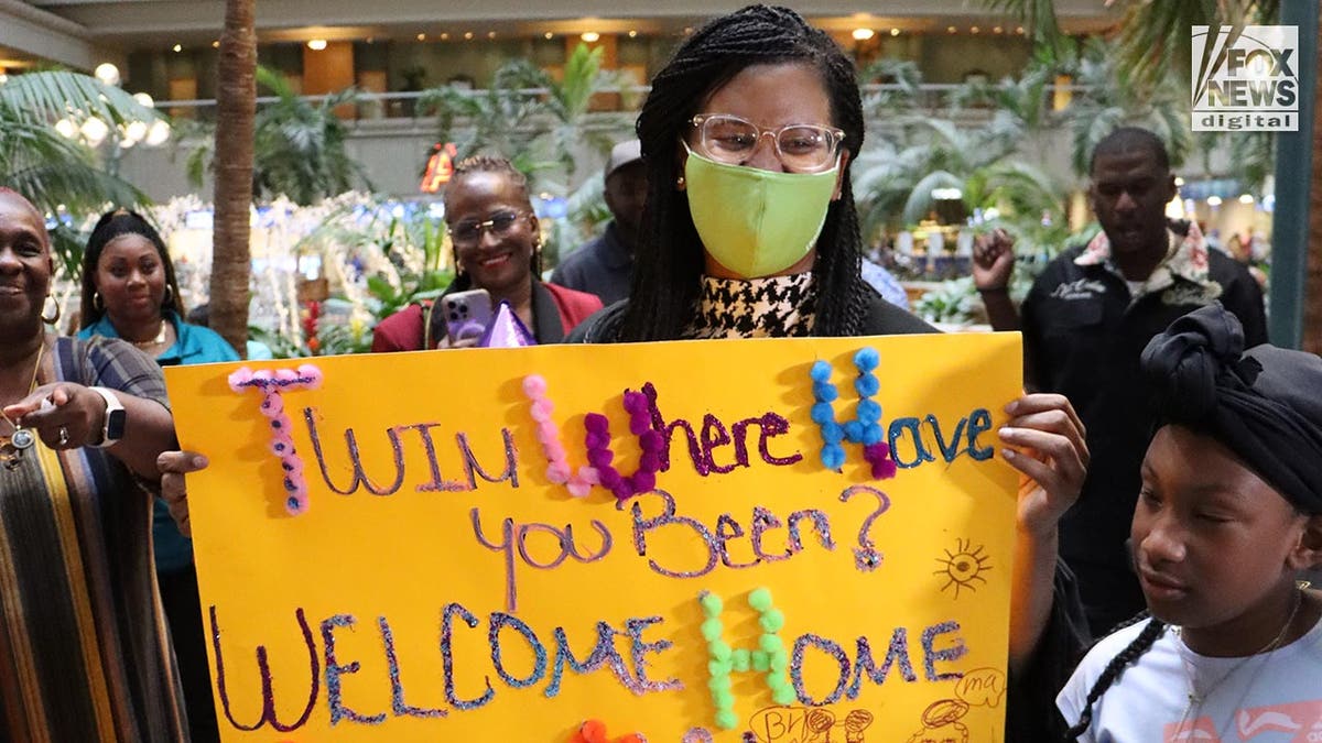 Sharitta Grier holds up a 'welcome home' sign at the airport