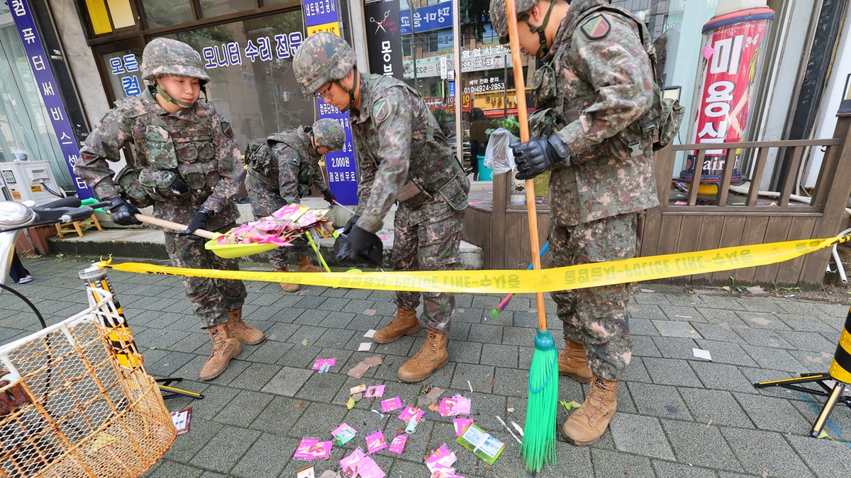 Soldados del ejército de Corea del Sur limpian basura detrás de una cinta de precaución amarilla.