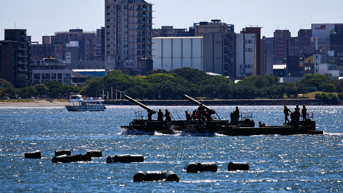Taiwanese soldiers stand on board an amphibious ferrying vehicle and release oil drums onto Tamsui River with the city of New Taipei in the background as part of the annual Han Kuang military drill.