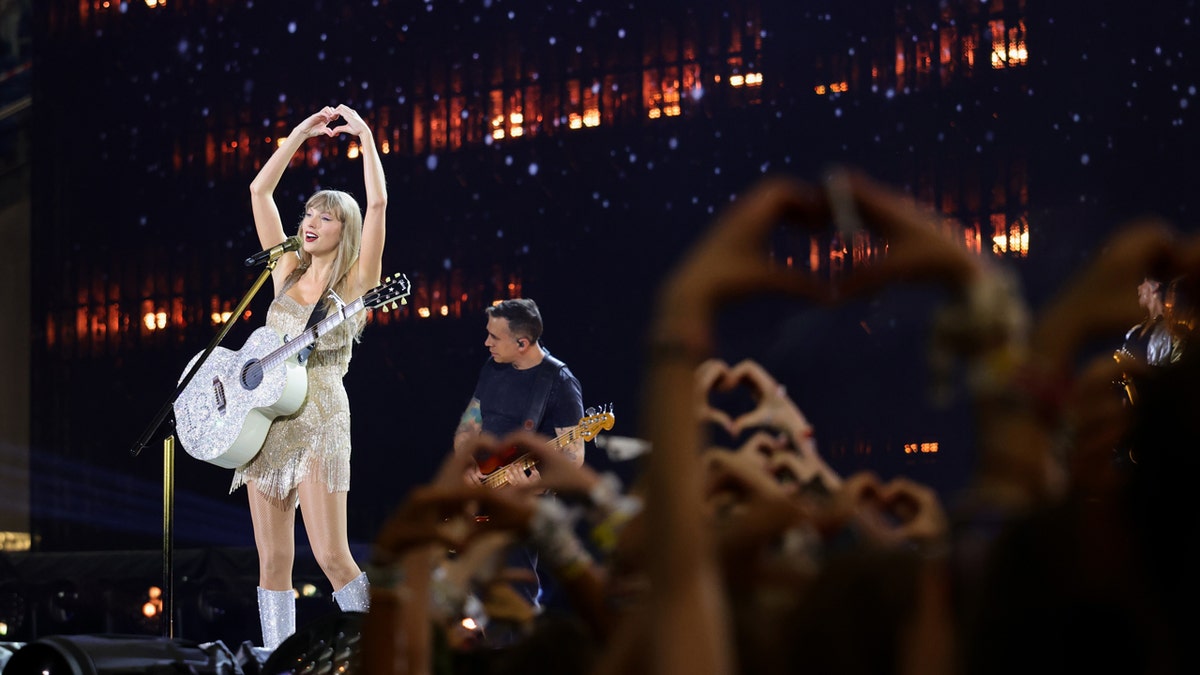 Taylor Swift holds up a heart with her hands
