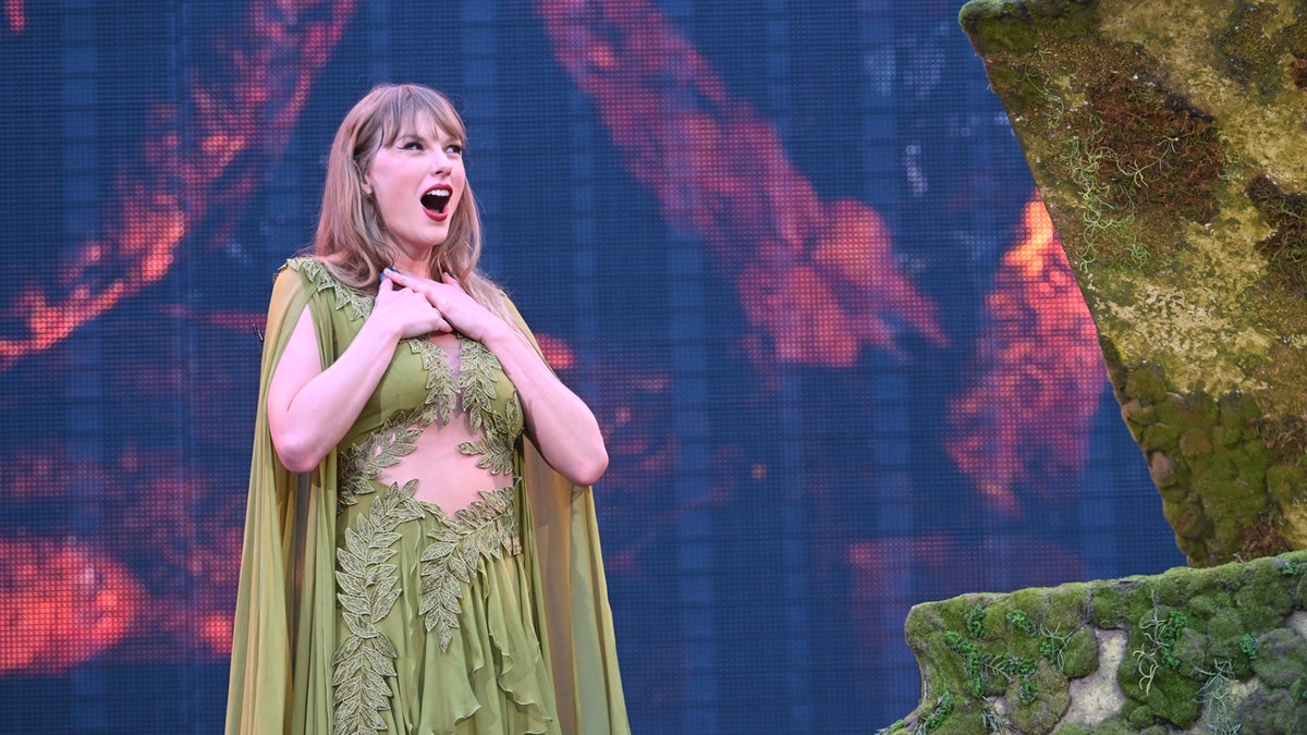Taylor Swift em um vestido verde sorri para a multidão durante a Eras Tour