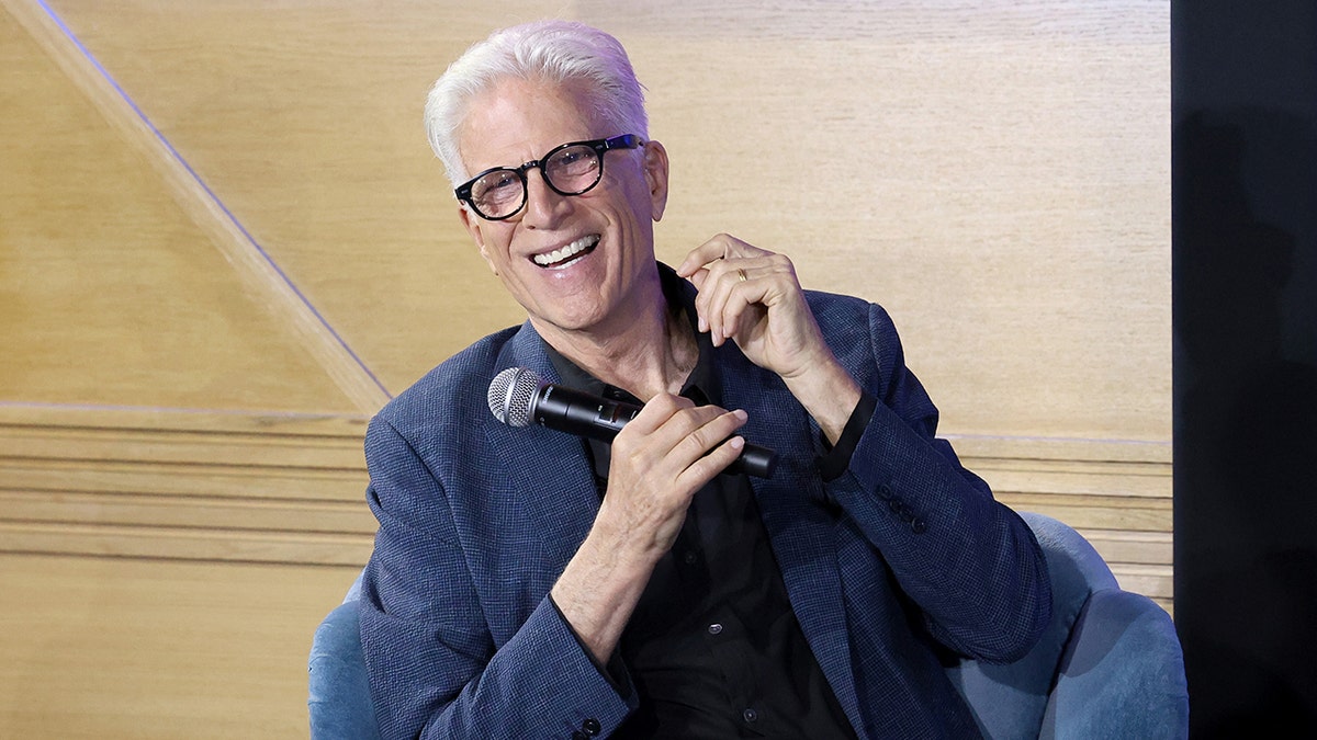 Ted Danson smiling and laughing while holding a microphone