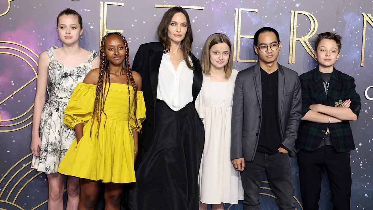 Angelina Jolie in a black outfit poses with 5 of her 6 kids on the carpet