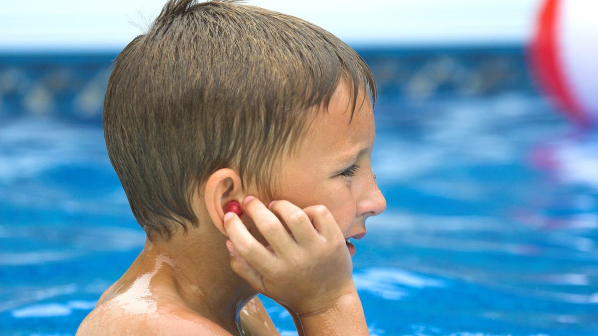 A young boy in the pool with an earplug