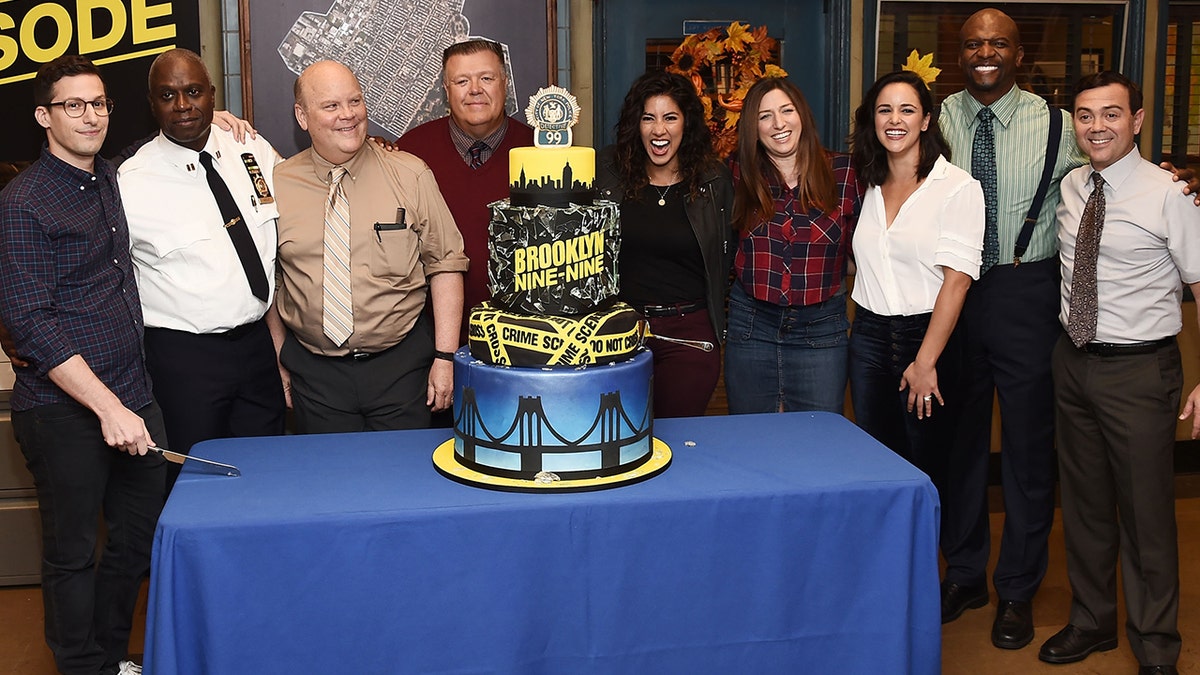 Andy Samberg and the rest of the "Brooklyn Nine-Nine" cast around a cake.