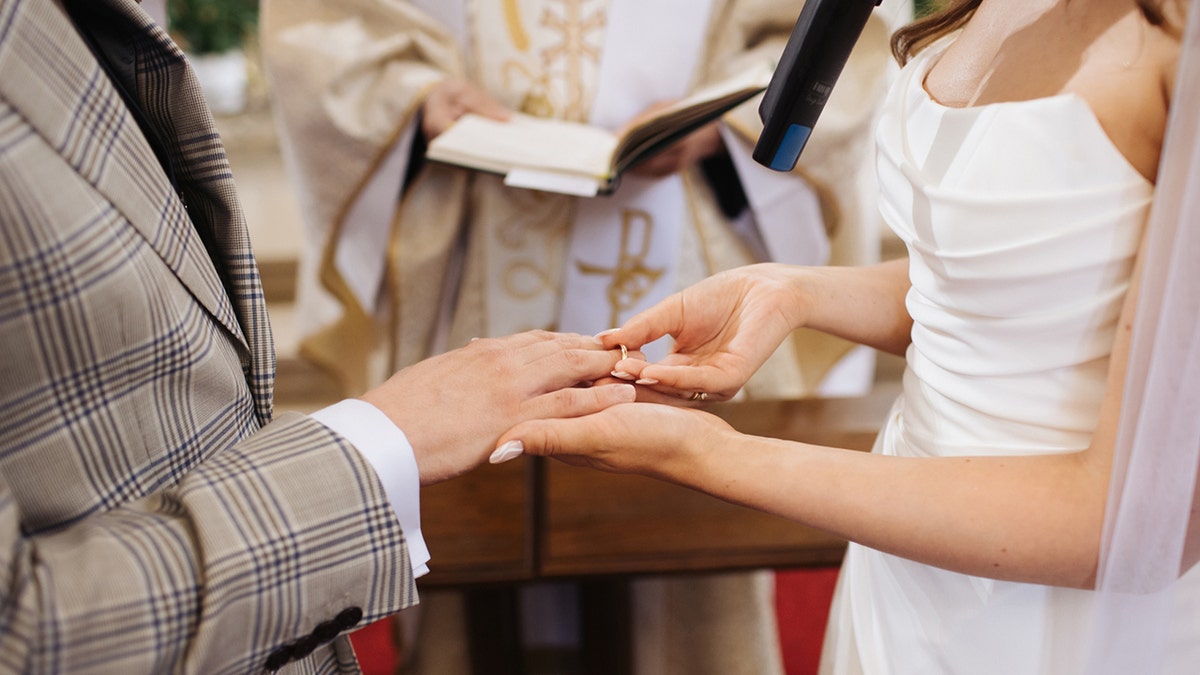 A bride putting a wedding ring on groom's finger during church ceremony